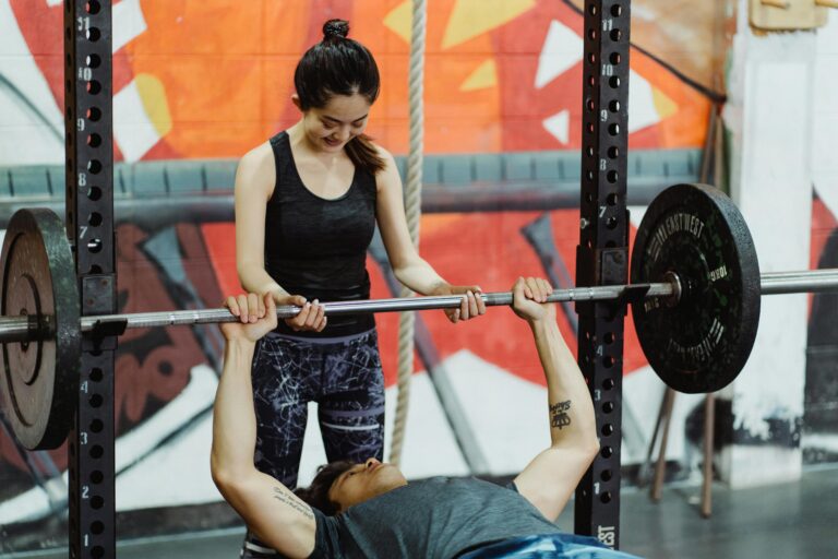 Woman assisting man during bench press exercise in colorful gym setting.